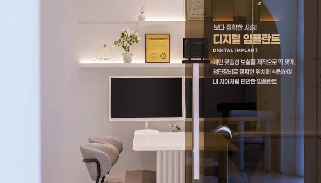 상담실 안의 모니터와 의자, 선반에 놓인 액자, 유리벽에 디지털 임플란트 안내 문구가 붙어 있다
