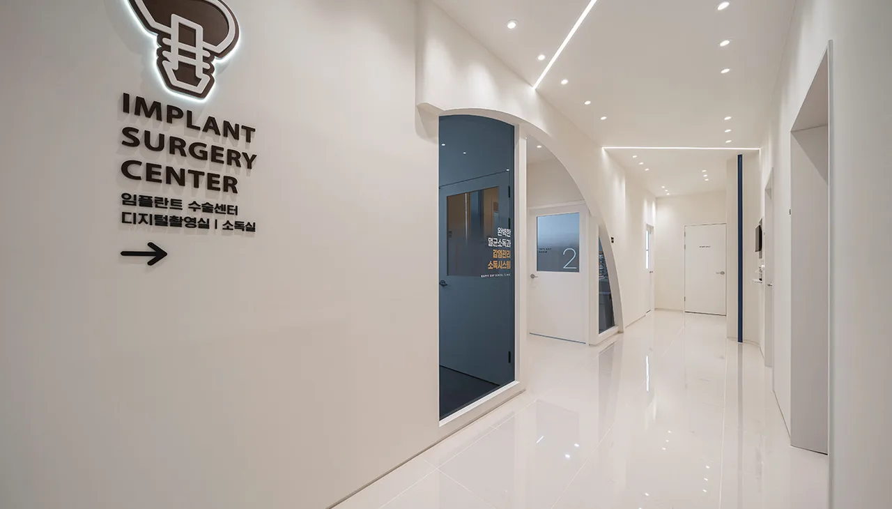 복도 벽에 IMPLANT SURGERY CENTER 표지와 임플란트 수술센터·디지털촬영실·소독실 안내가 붙어 있고 옆에 남색 아치 문이 있다